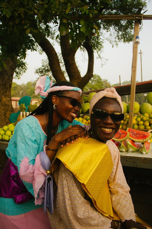 Two smiling market vendors behind a stall of watermelons